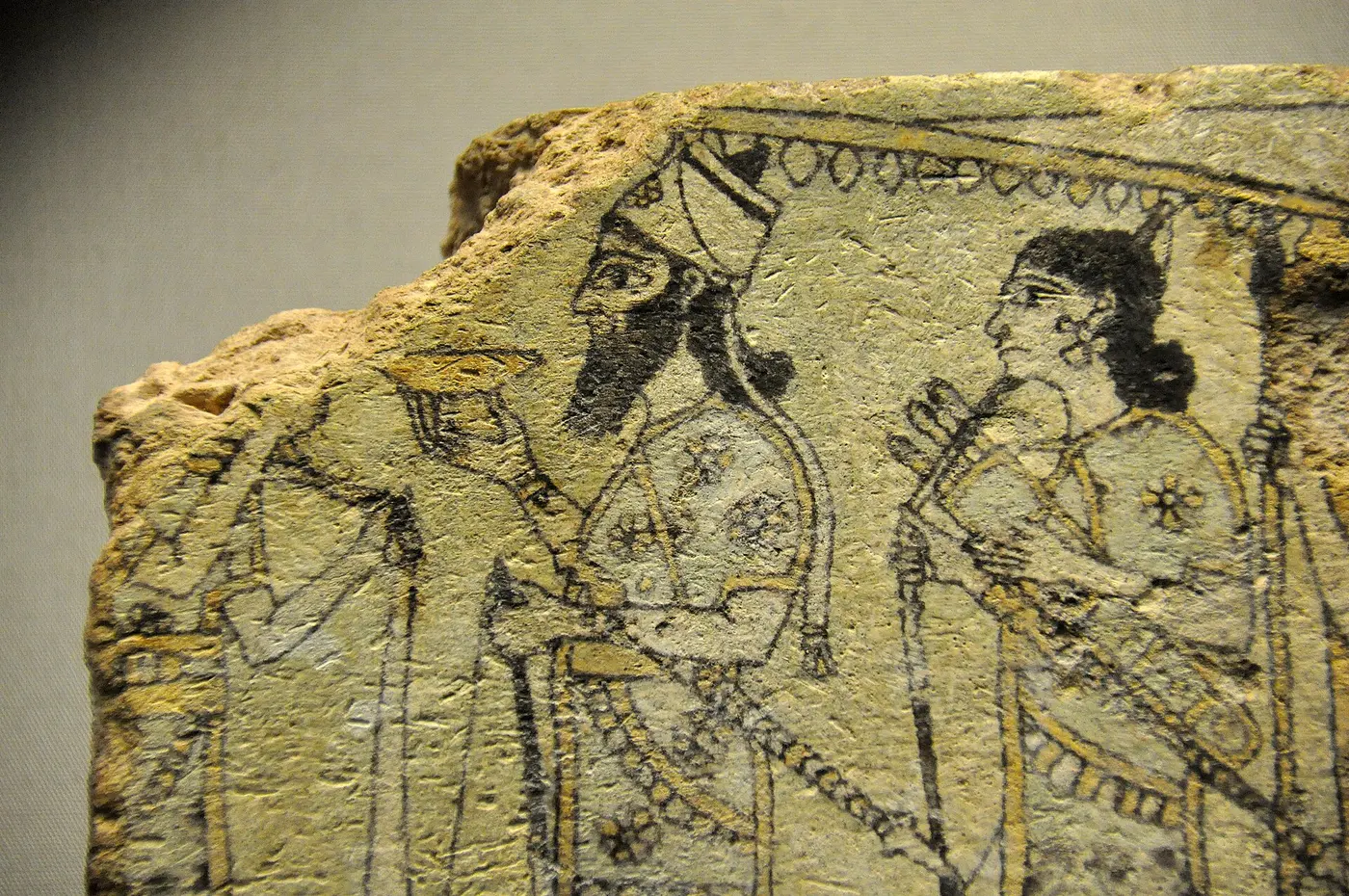 An ancient painted tile showing a king raising a cup beneath a fringed parasol, surrounded by attendants