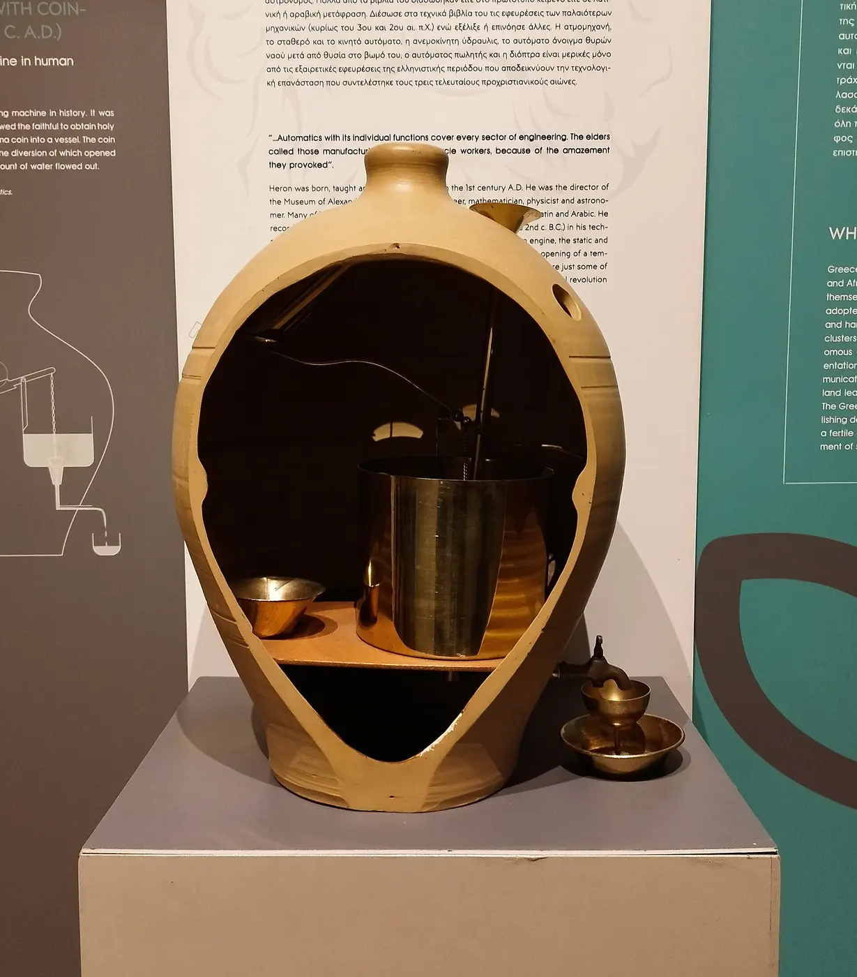 An earthenware jar with a large section of its side cut away, revealing a metal container and a lever mechanism inside, with a bowl under a spout outside