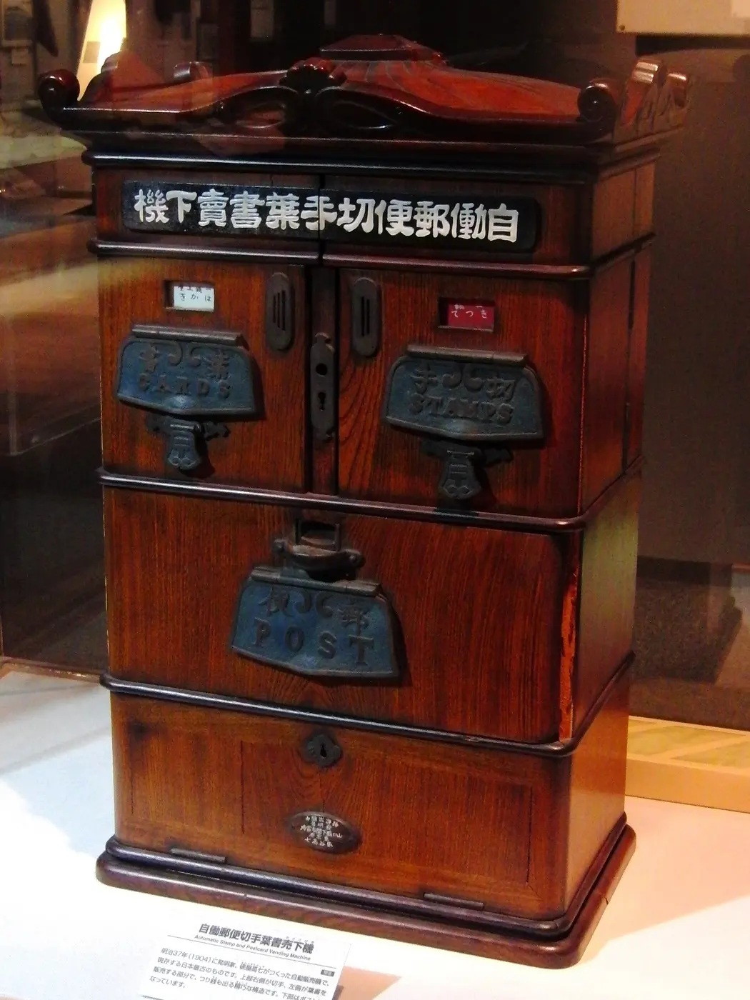 A wooden cabinet labeled with the machine’s Japanese name, with postcard and stamp outlets on the left and right and a mail slot below