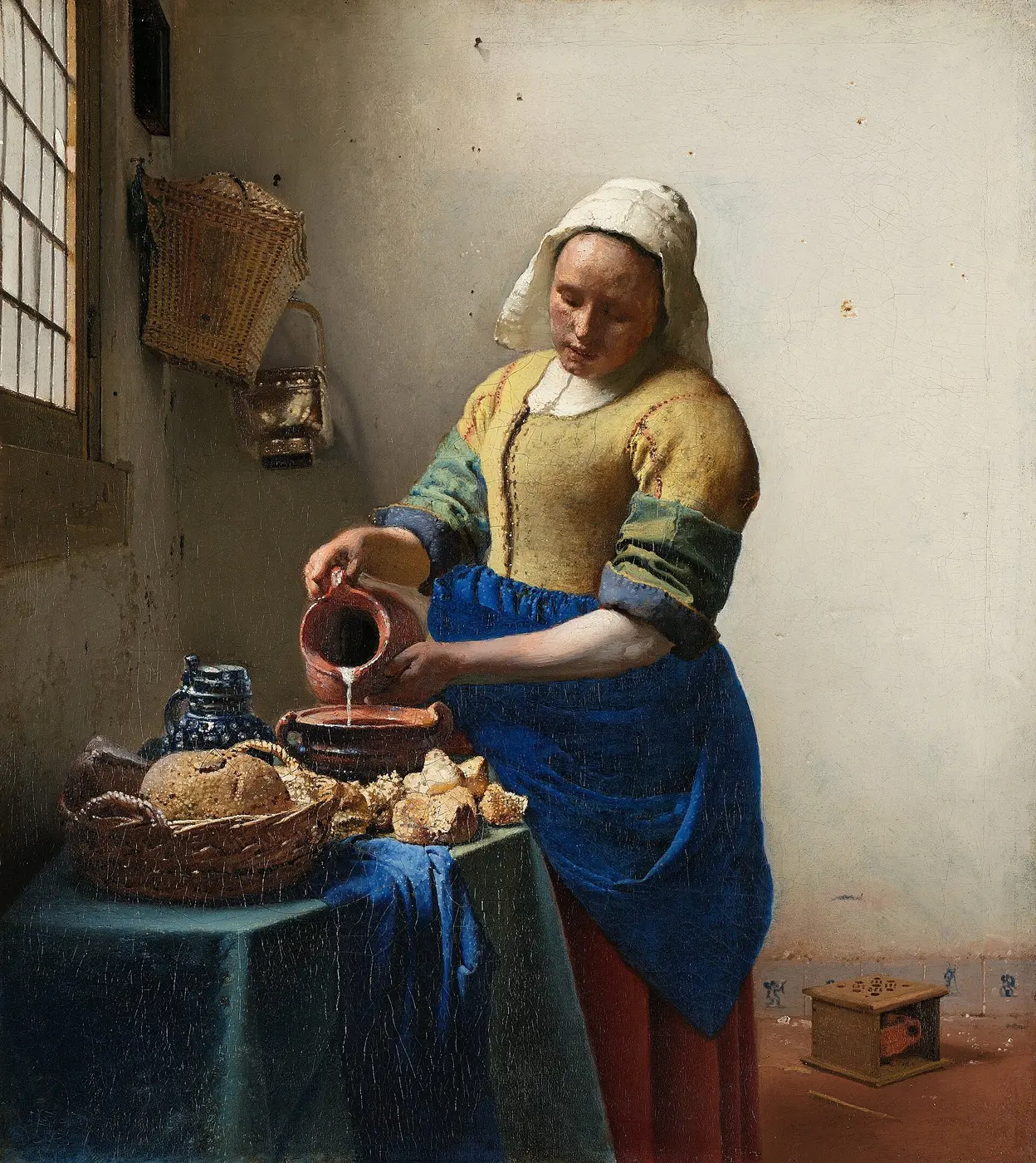 An oil painting of a woman in a yellow bodice and blue apron pouring milk from a jug into a bowl on a table, in a kitchen lit by a window