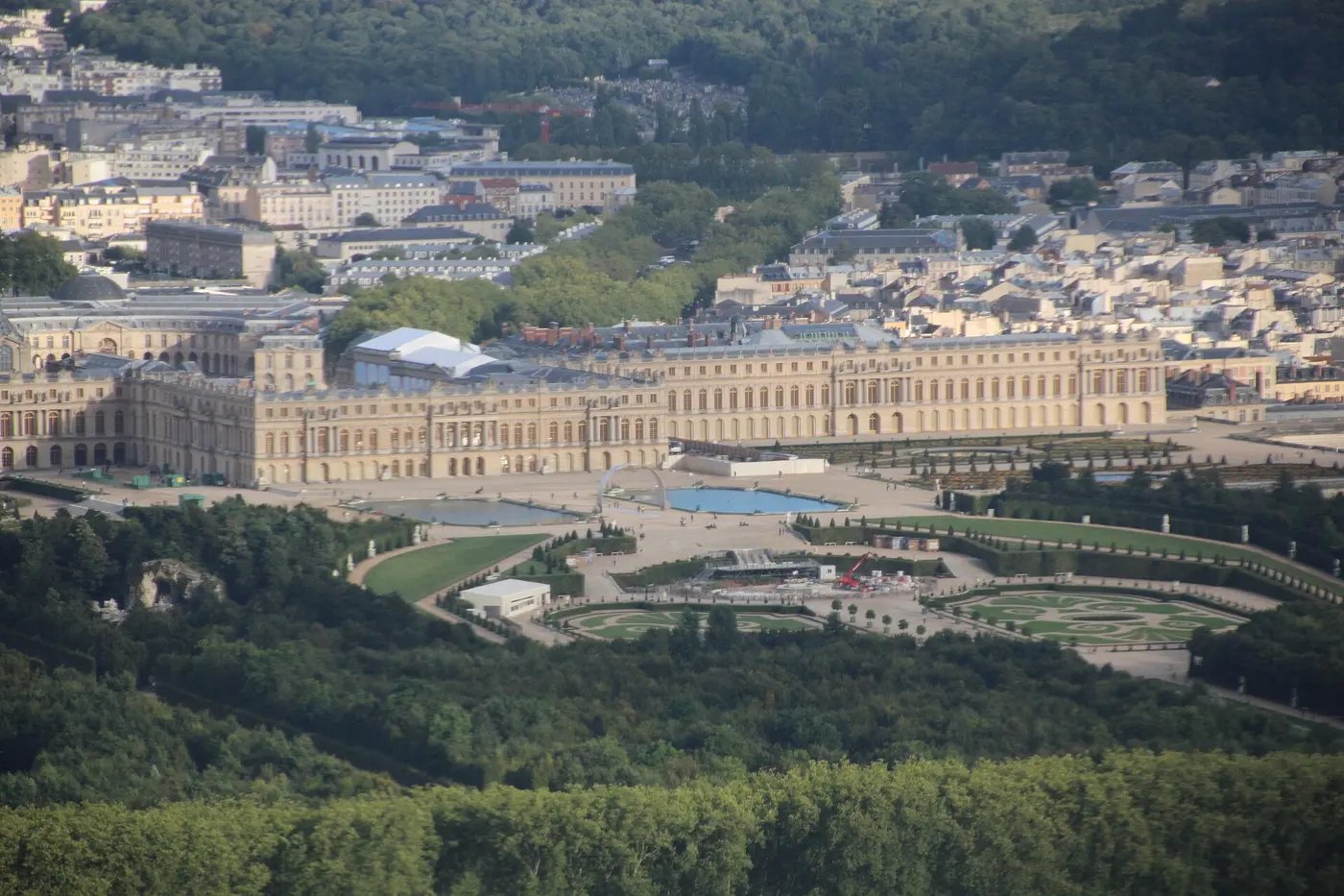 Aerial view of the long palace building beyond woods and geometric gardens