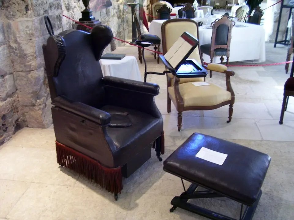 A leather-upholstered armchair with a hole in the seat, next to a footstool