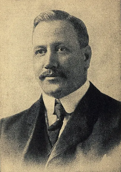 Portrait photograph of a man with a moustache, wearing a suit and tie