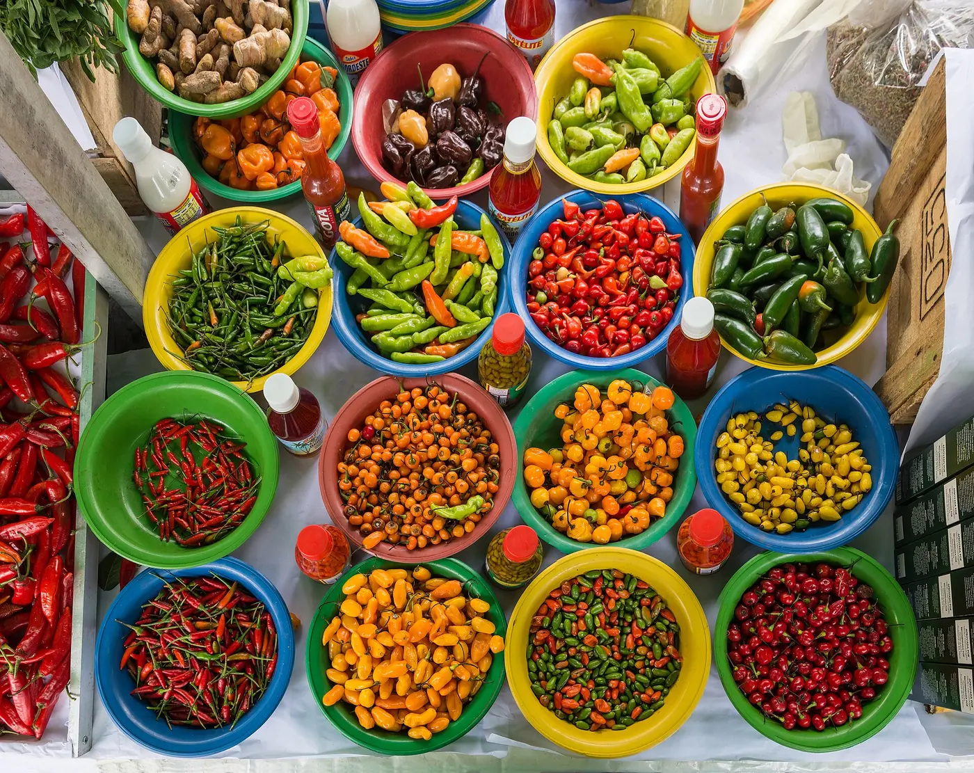 Chili peppers of many shapes and colors piled into colorful containers