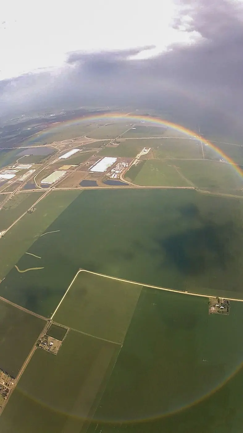 A photo looking down over farmland, with a rainbow forming an almost complete ring