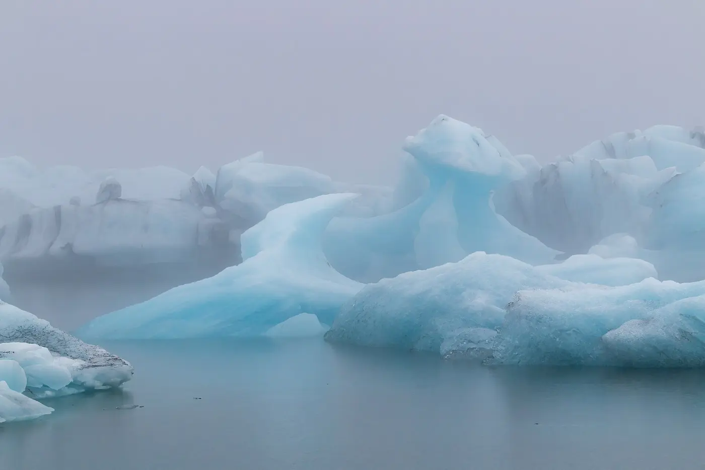Pale blue icebergs floating in a misty lagoon