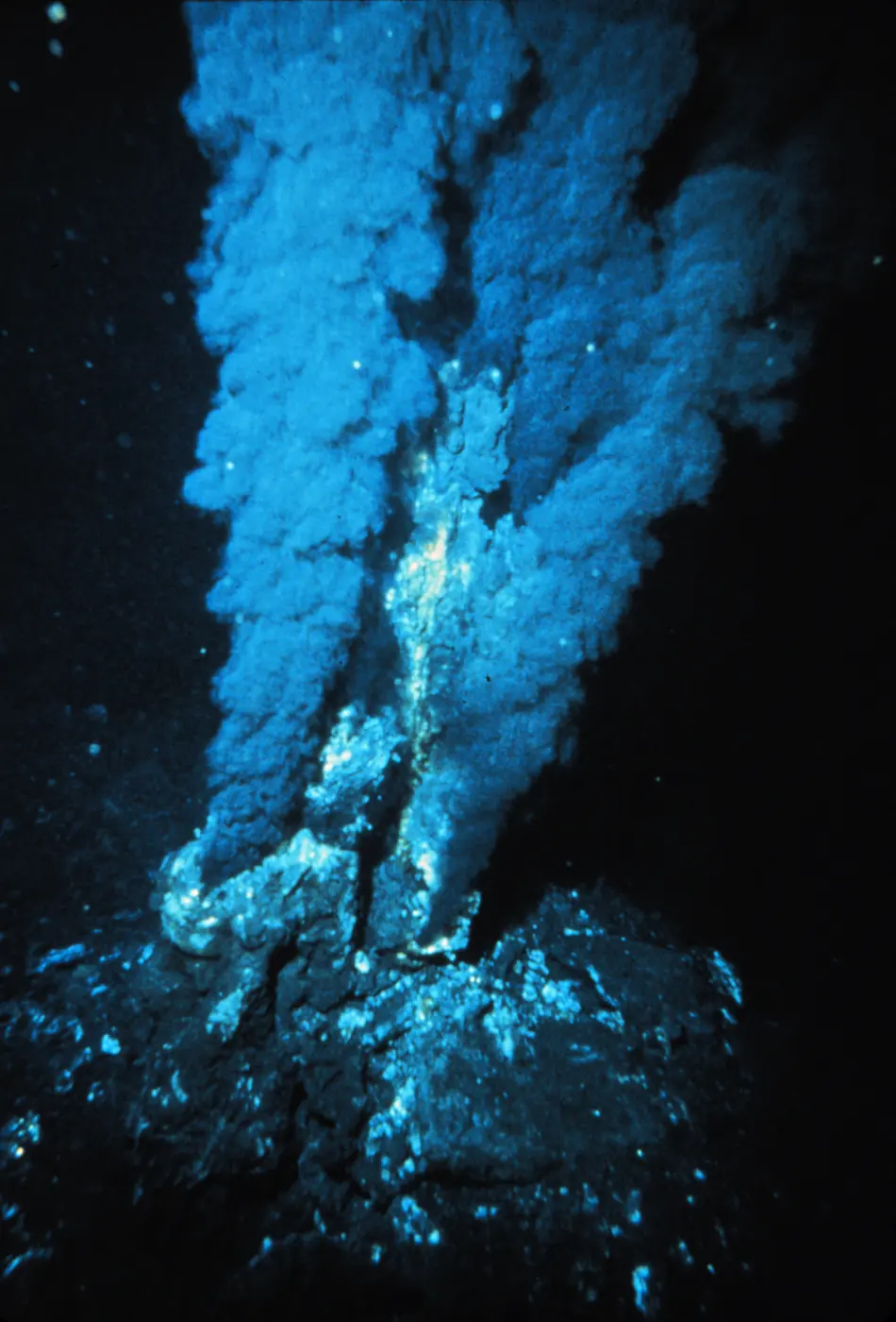 Billowing, smoke-like hot water pouring from a rocky chimney on the dark seafloor
