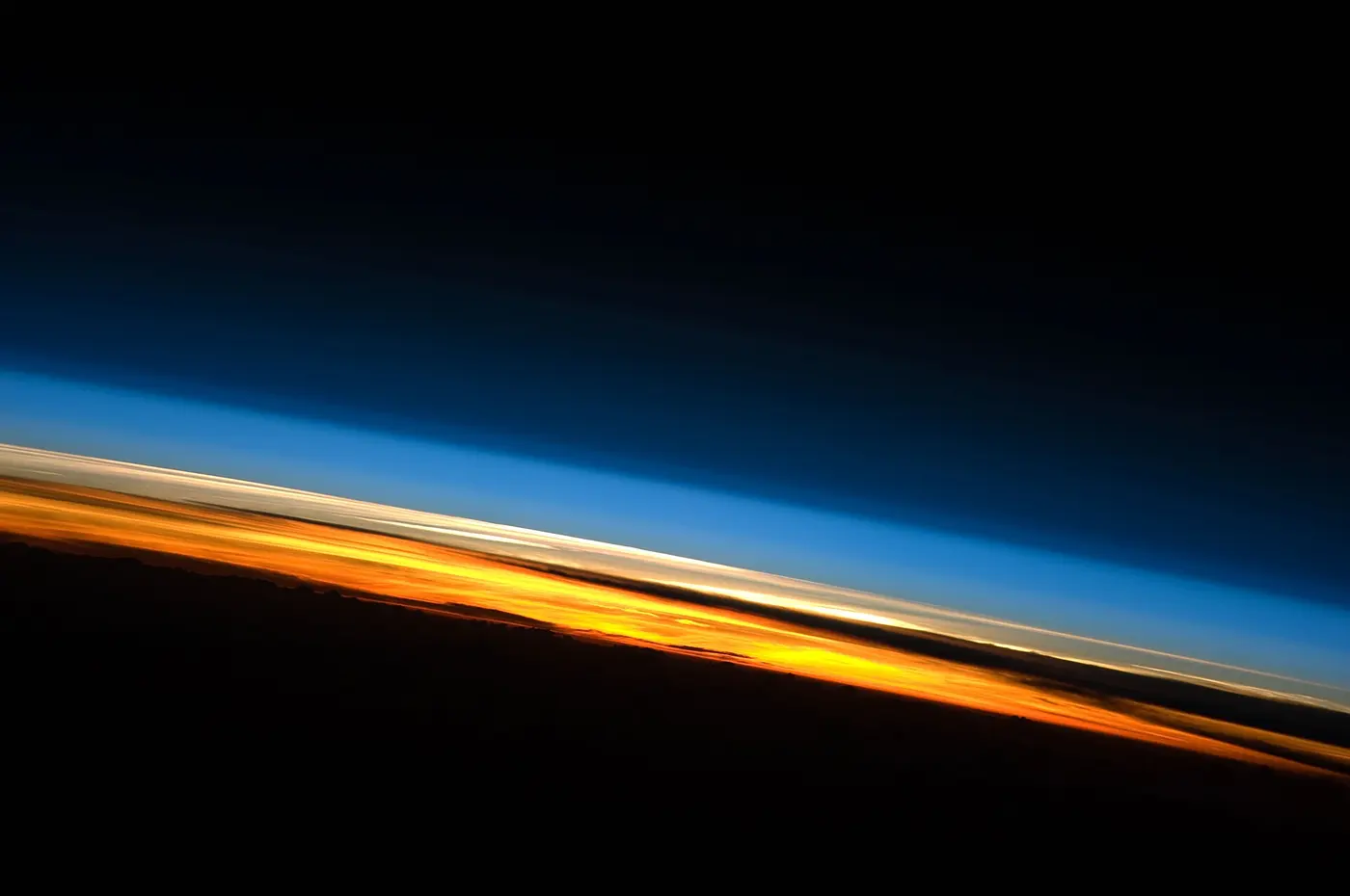 Bands of orange, white and blue layered along Earth’s horizon against the black of space