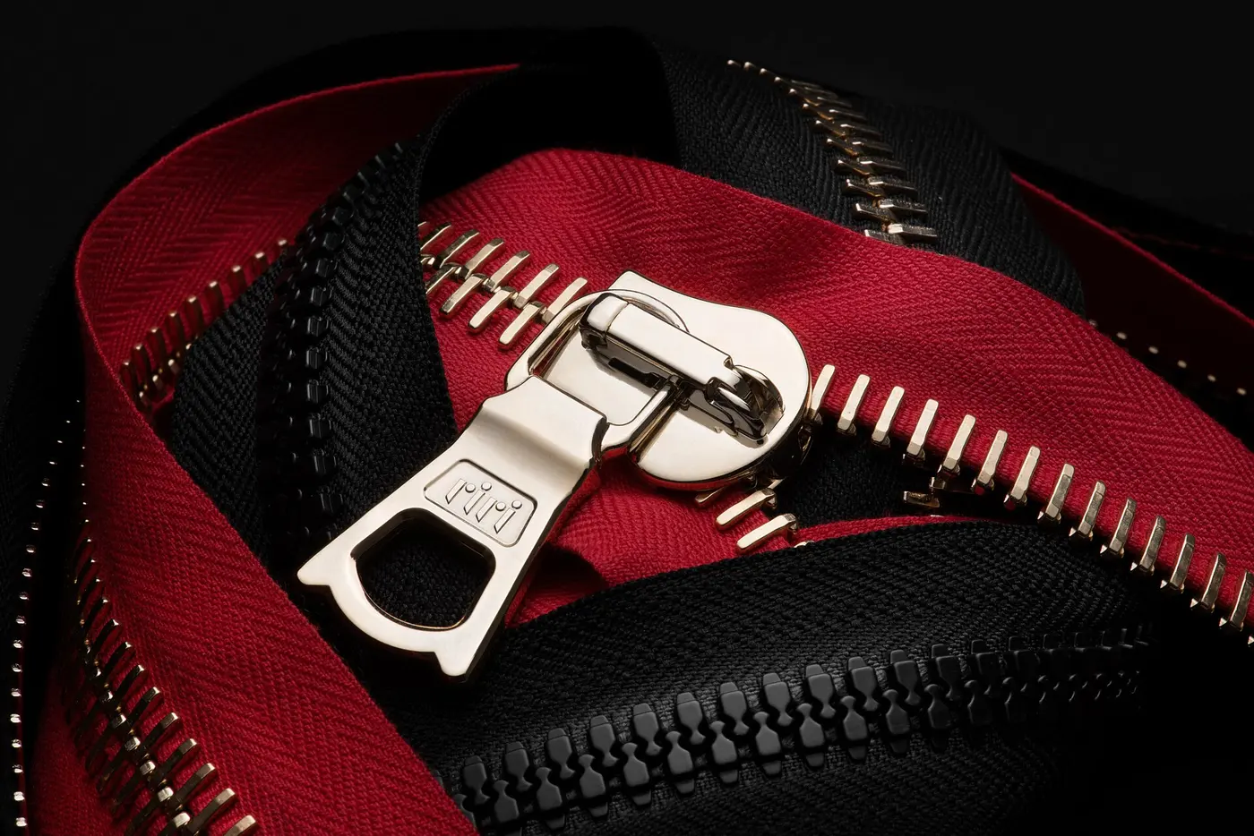 Metal teeth lined up on red and black fabric tape, with a silver slider
